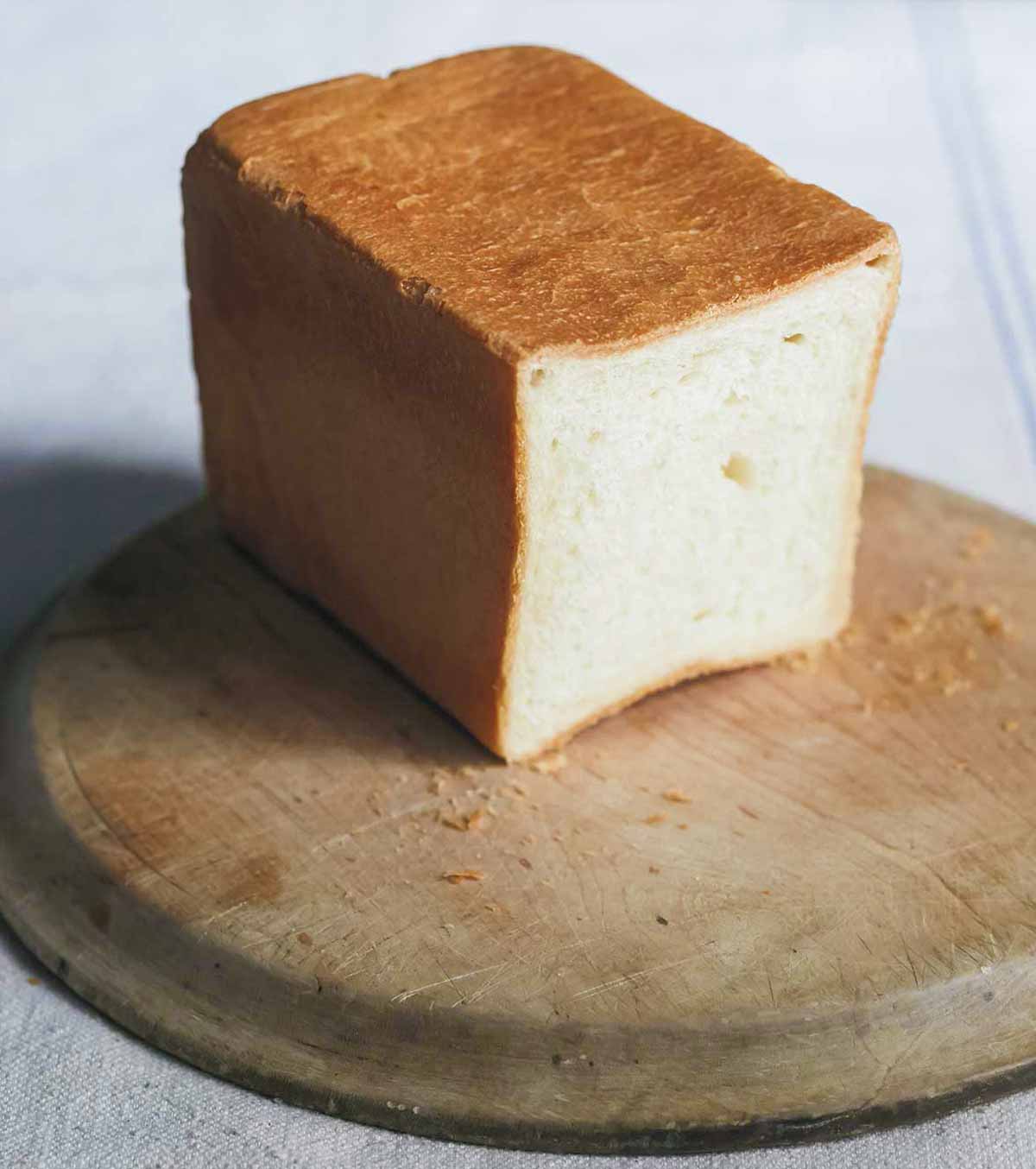 Part of a loaf of pain de mie on a round wooden cutting board.