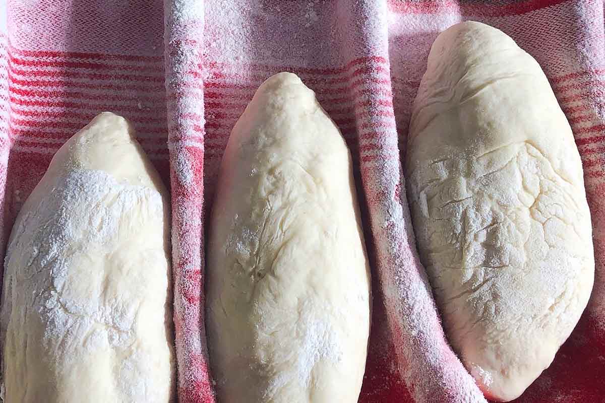 Three unbaked papo-secos rising on a ridged towel.