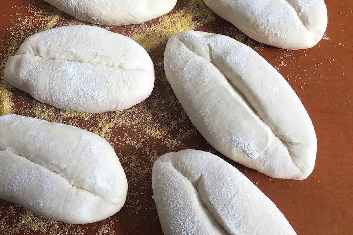 Unbaked papo-secos on a cornmeal-dusted baking mat.