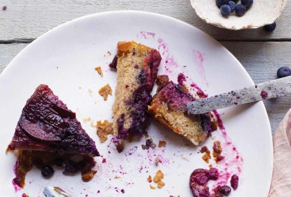 A couple slices of plum-blueberry upside-down cake on a white plate with a knife resting on the edge of the plate.