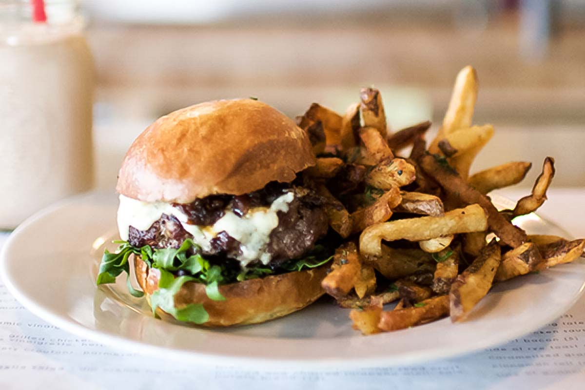 A skillet cheeseburger with arugula and a pile of fries on a white plate.