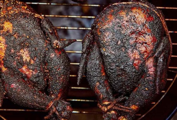 Three whole smoked chickens on a round grill.