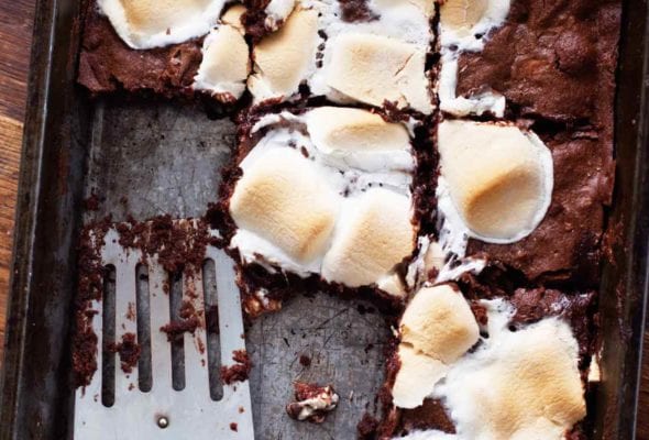 A tray of s'mores brownies with a spatula resting inside and several brownies missing.