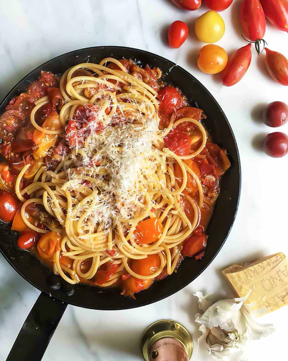 A black skillet filled with summer tomato pasta, sprinkled with fresh Parmesan cheese.