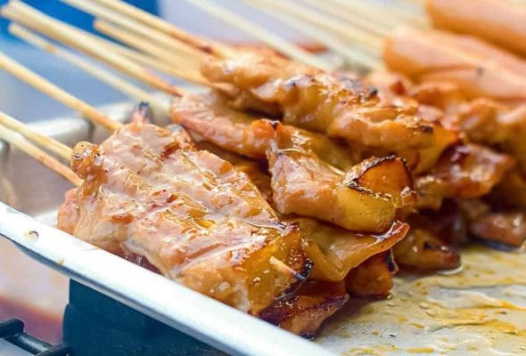 Skewers of thinly sliced Thai-style grilled pork skewers on a metal tray in a street food vendor's cart