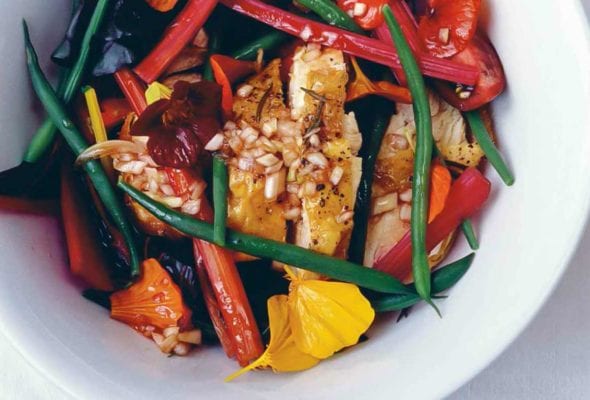 A white bowl filled with warm chicken with green beans and chard, topped with edible flowers.