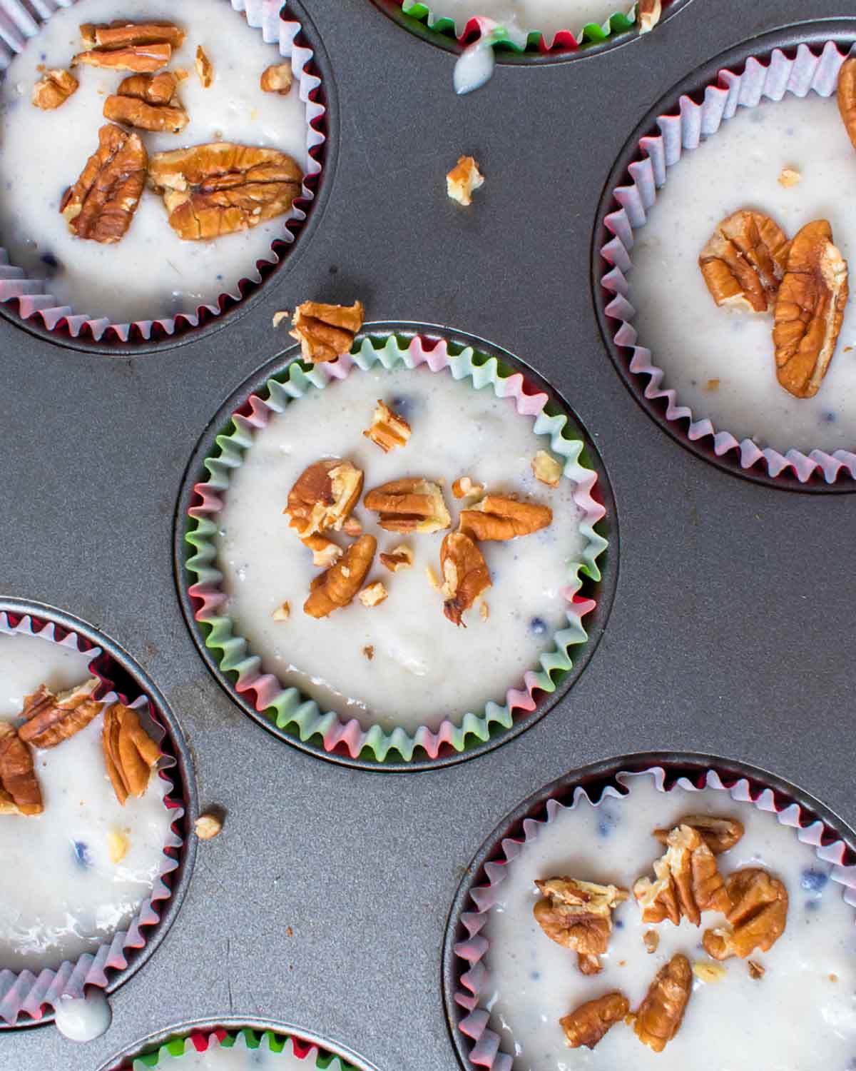 Unbaked blueberry pecan muffins in a muffin tin with pecans scattered on top.