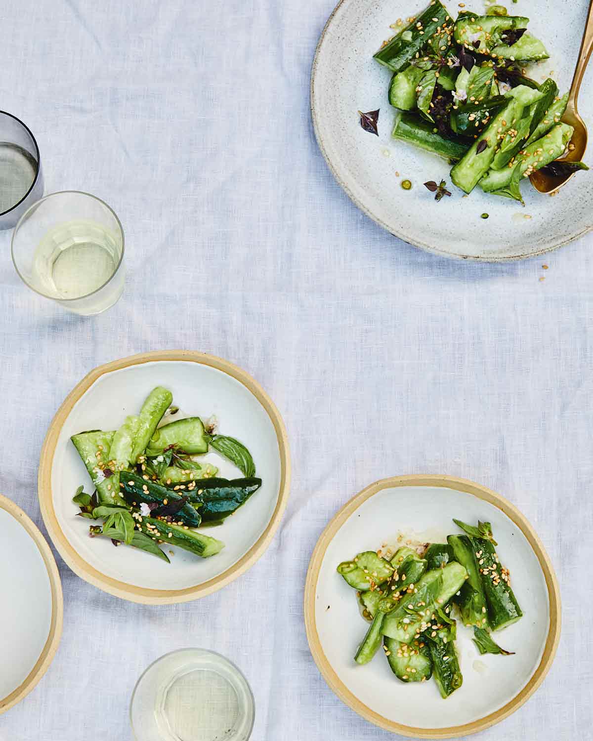 A serving plate and several individual plates topped with Chinese smashed cucumber salad.
