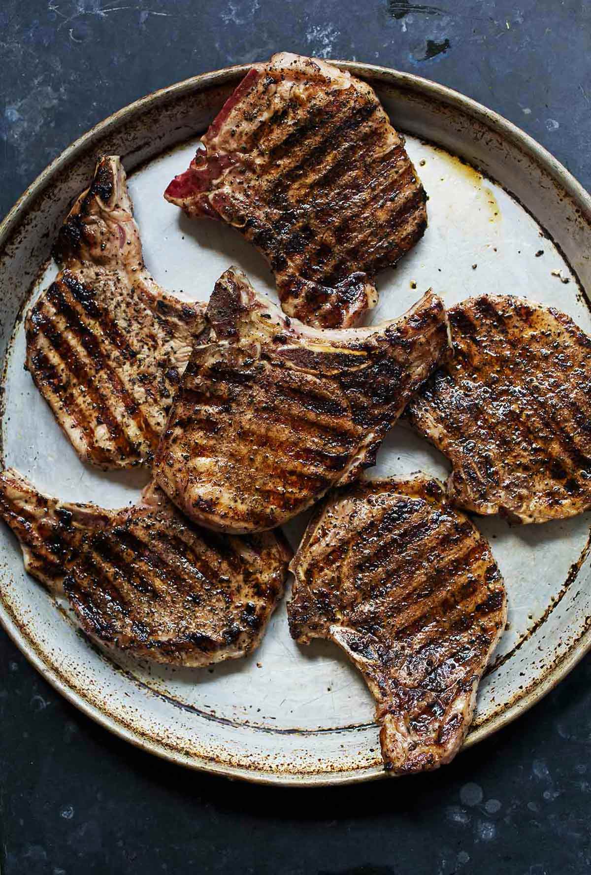 Six coffee-crusted grilled pork chops on a speckled platter.