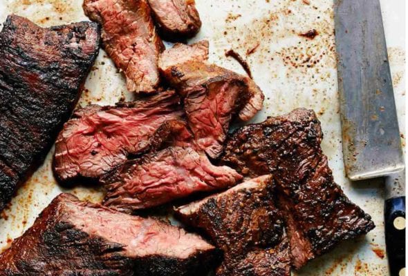 A sliced grilled steak with coffee spice rub and a carving knife lying beside it