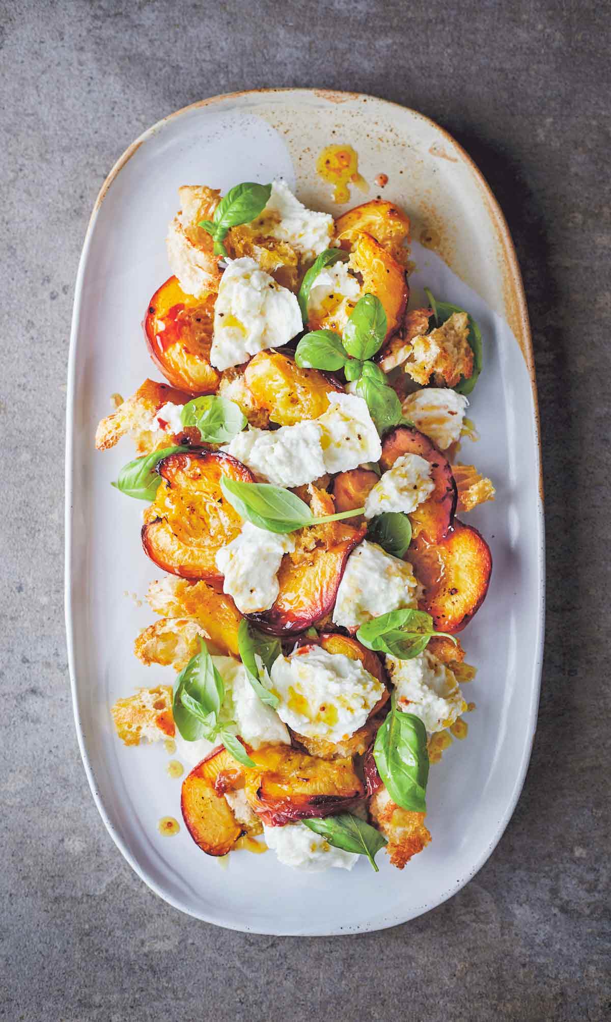 A white oval platter topped with fresh mozzarella with roasted stone fruit and toasted bread pieces.