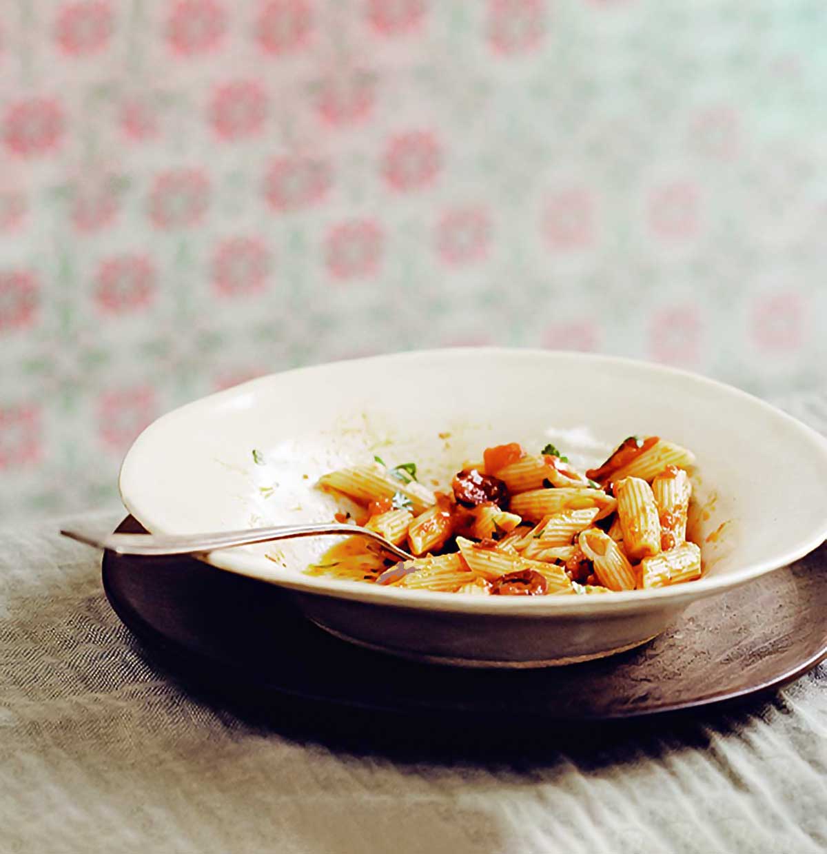 White bowl with ziti and a pasta puttanesca sauce
