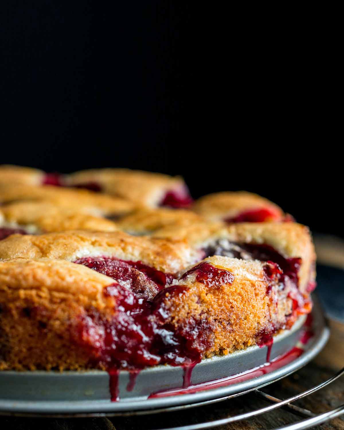 A purple plum torte with dripping juice on a baking pan, all on a cooling wrap