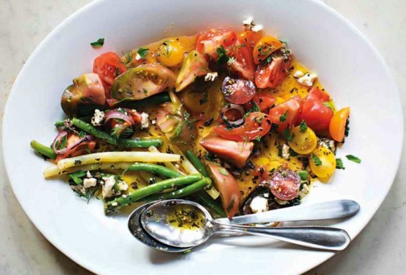 White plate of tomato and green bean salad with feta, red onion, parsley, and mint