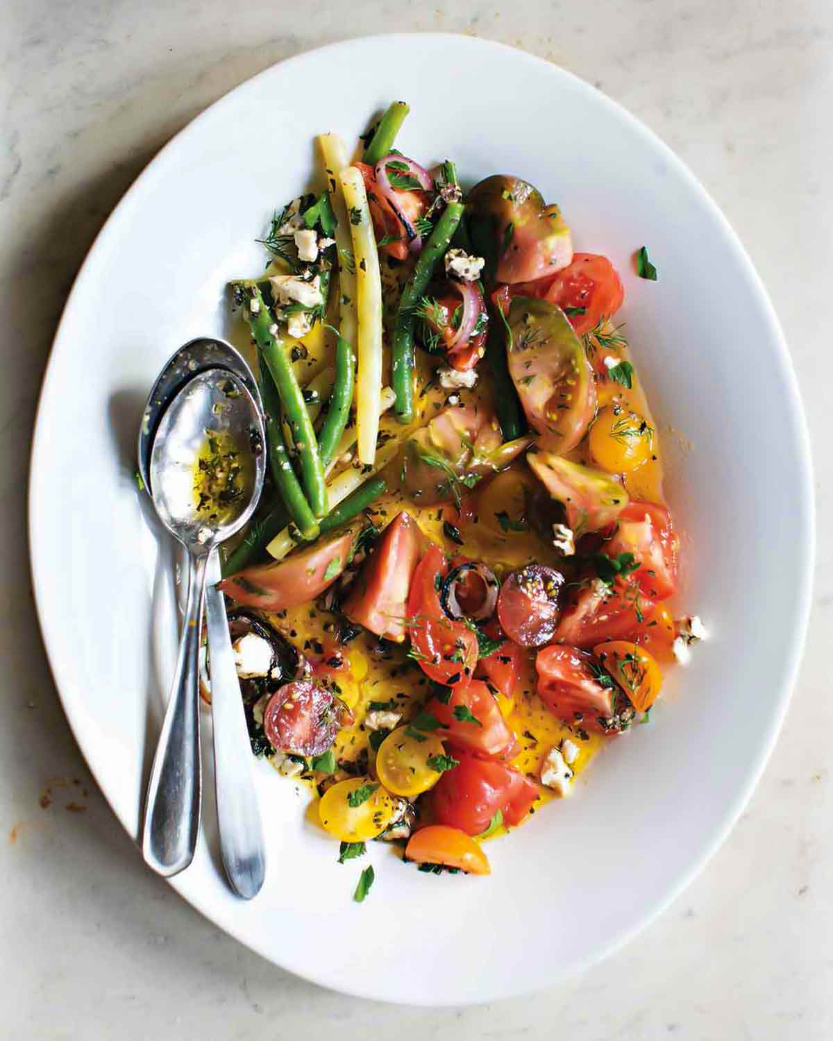 White plate of tomato and green bean salad with feta, red onion, parsley, and mint
