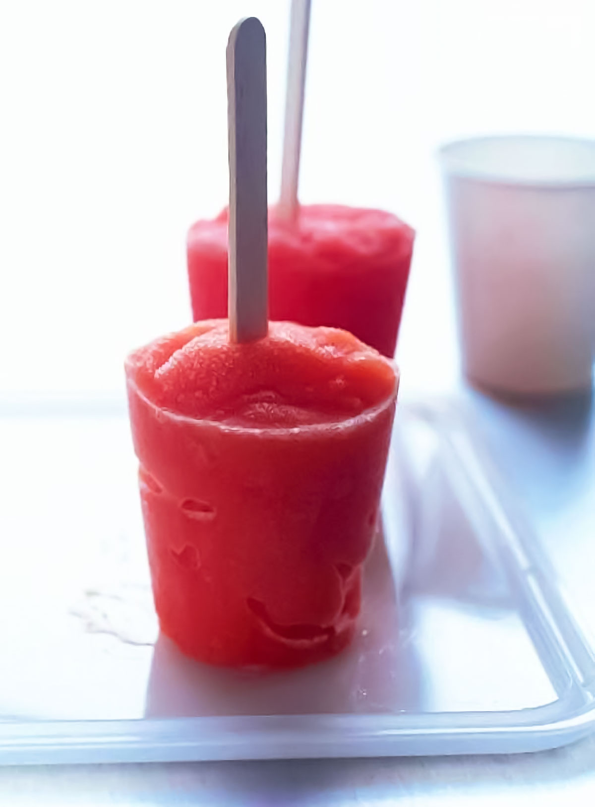 Two red tropical fruit popsicles on a plastic tray.