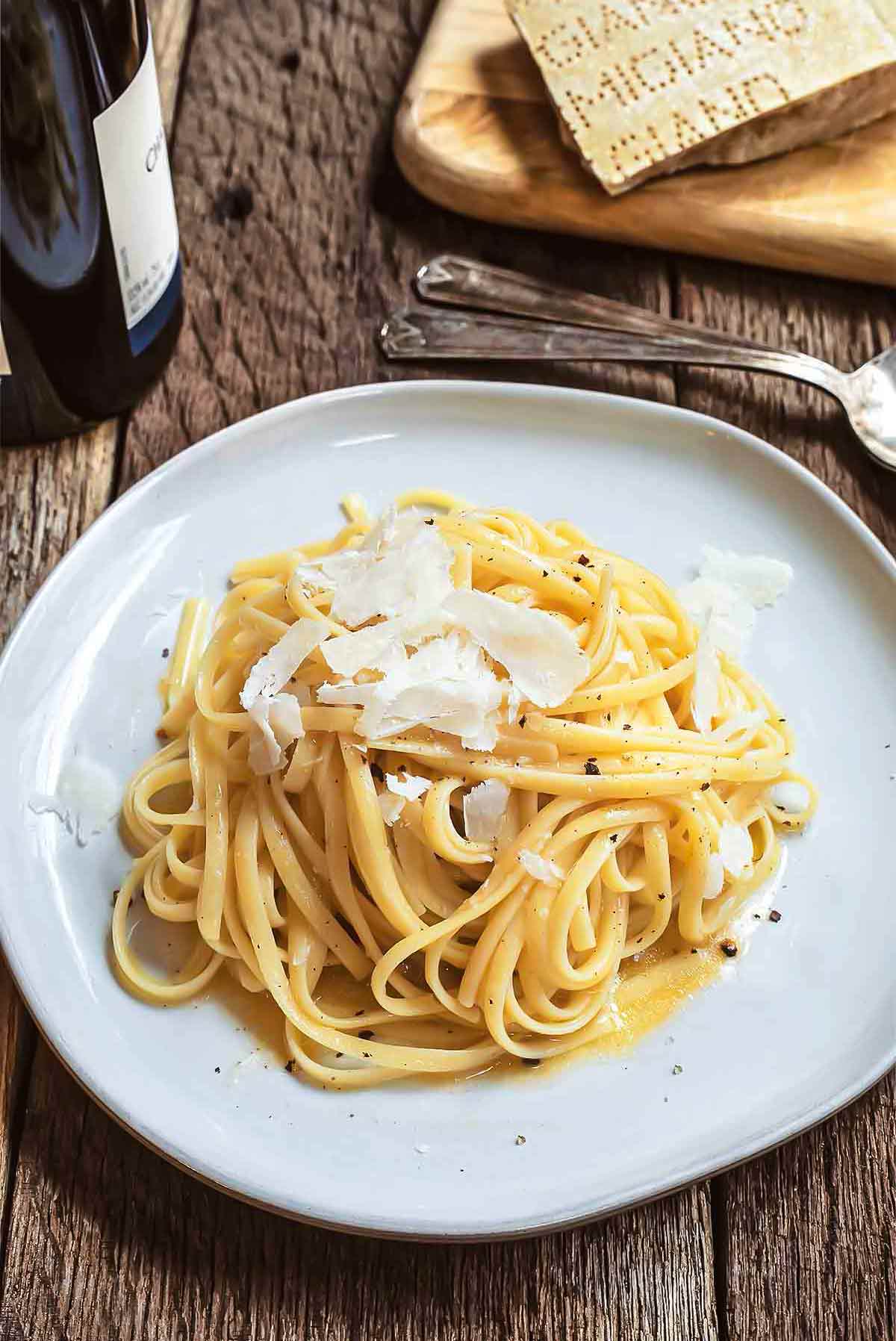 A tangle of white wine linguine on a white plate, topped with Parmesan.