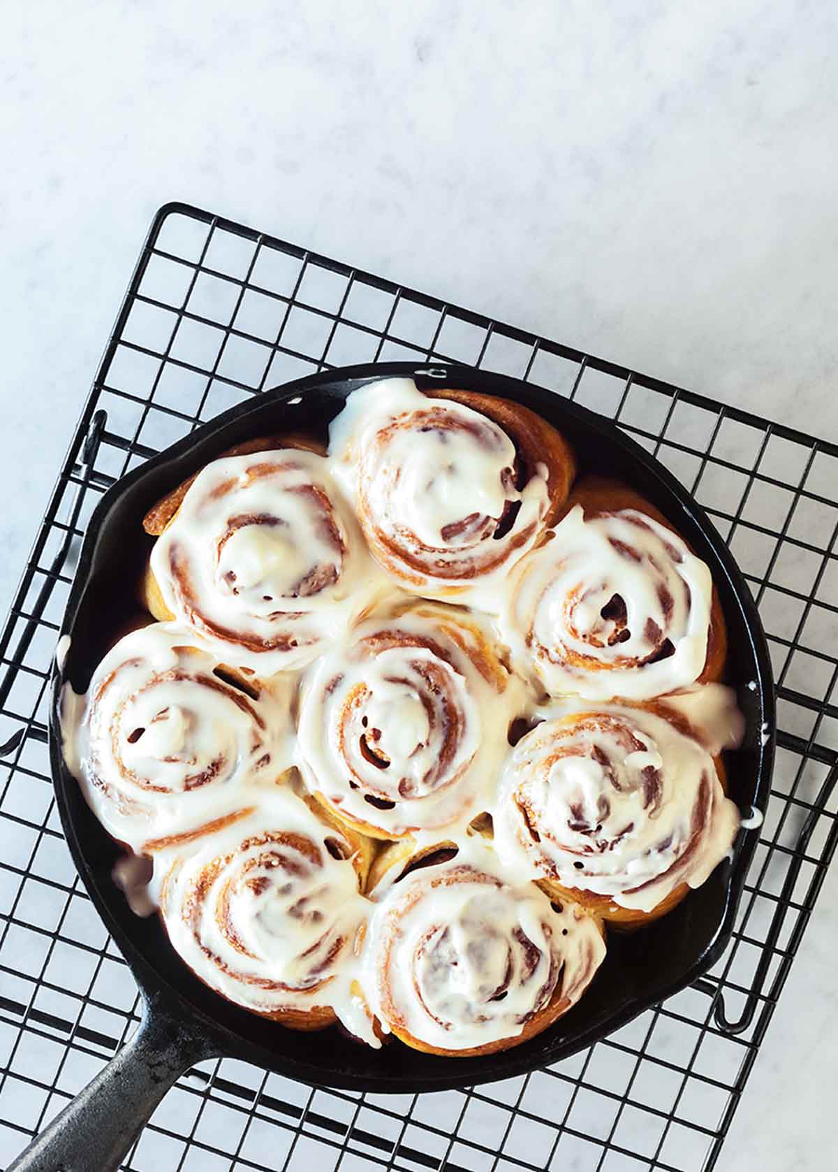 A cast-iron skillet filled with glazed biscuit cinnamon rolls on a wire rack.