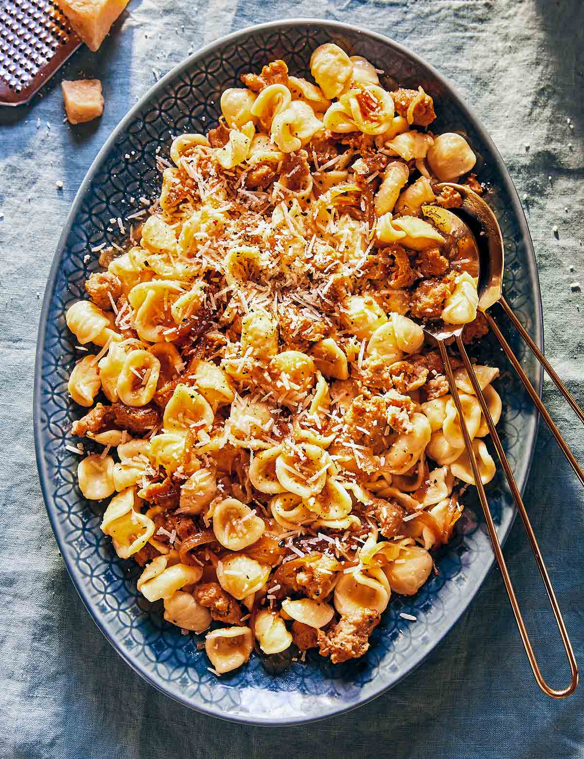 An oval serving dish filled with caramelized onion pasta and two large serving spoons nestled into it.