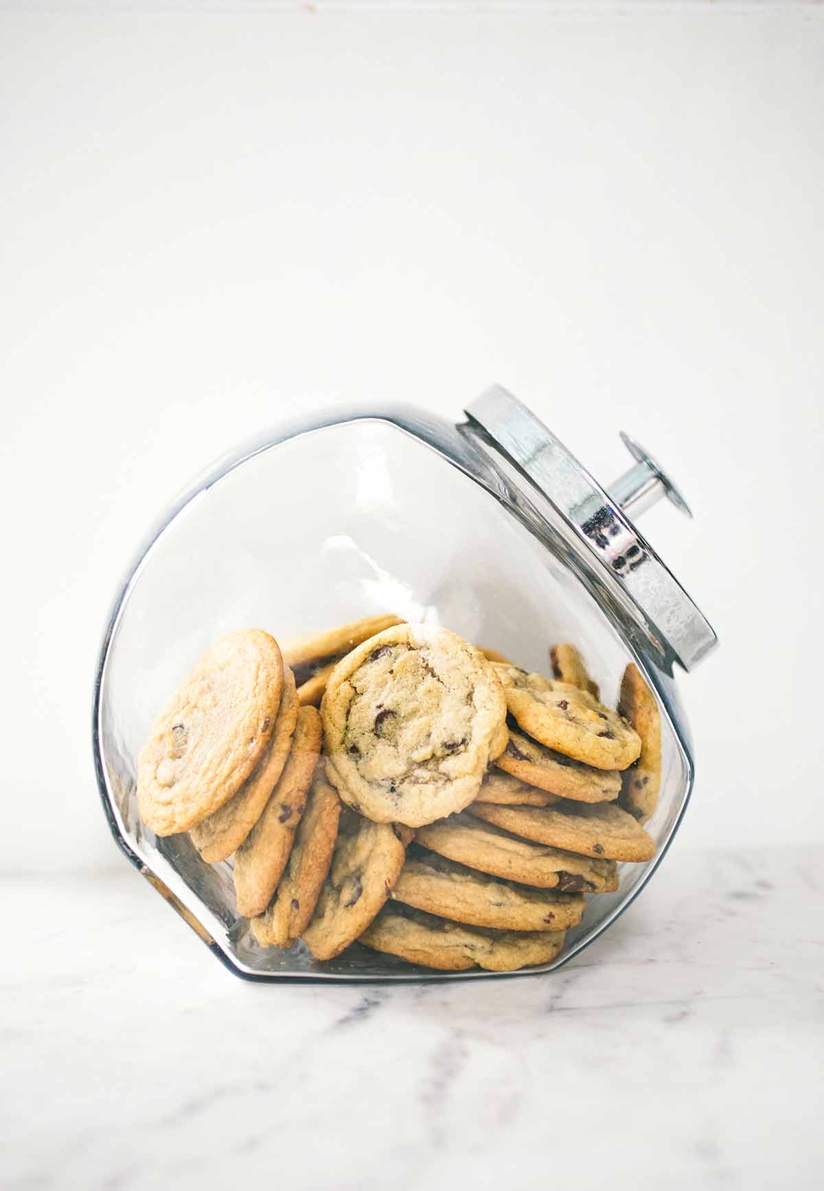 A glass jar filled with soft chocolate chip cookies.