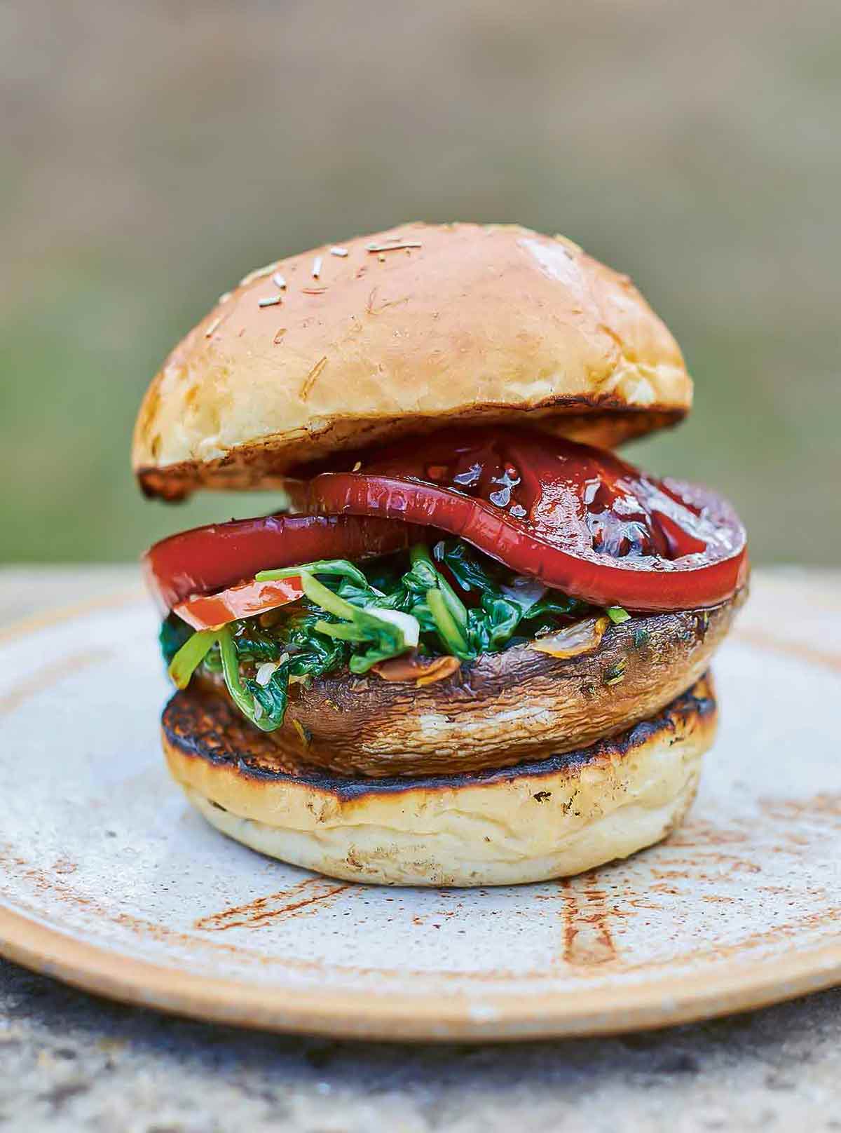 A spinach tomato mushroom burger between two toasted bun halves on a brown plate.
