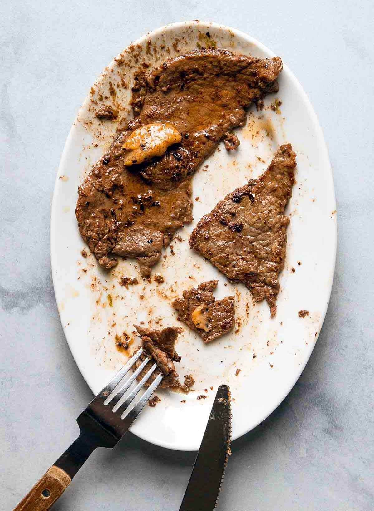 Two pieces of steak with chile-lime butter on an oval plate with a fork and knife cutting the steak.