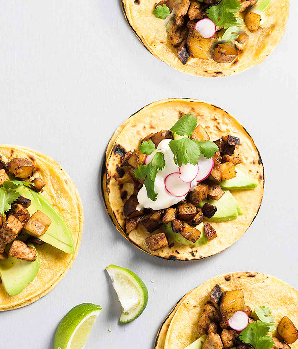 Four ancho pork and potato tacos topped with cubed pork and potatoes, sliced radish, sour cream, and cilantro.