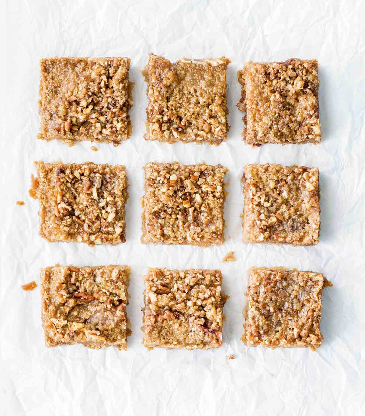 Nine apple crumb bars on a white sheet.