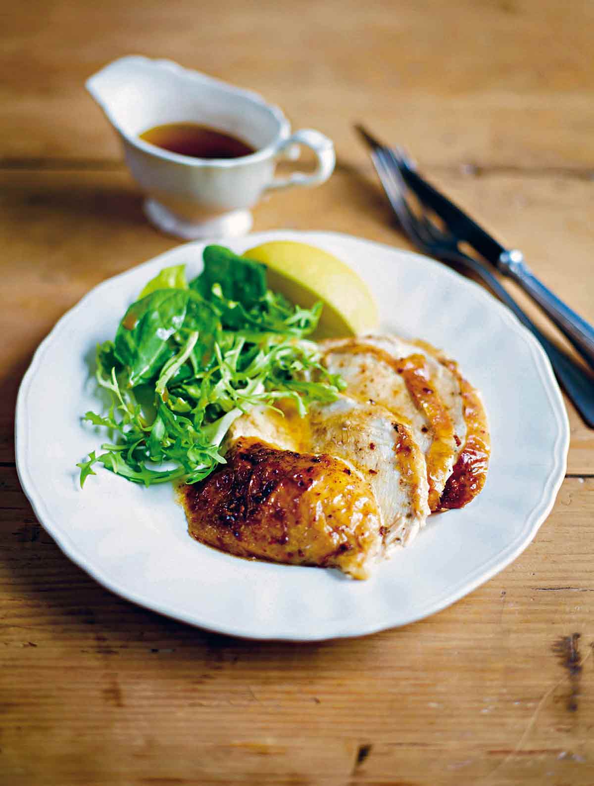 Plate of slices of baked chicken drizzled with cinnamon butter, green salad, and lemon wedge