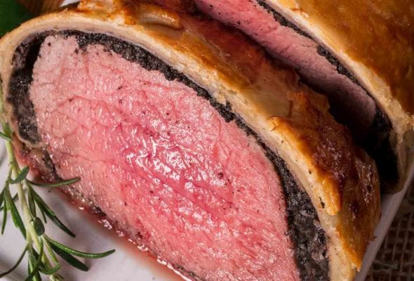 Close-up of a beef Wellington on a plate with a sprig of rosemary
