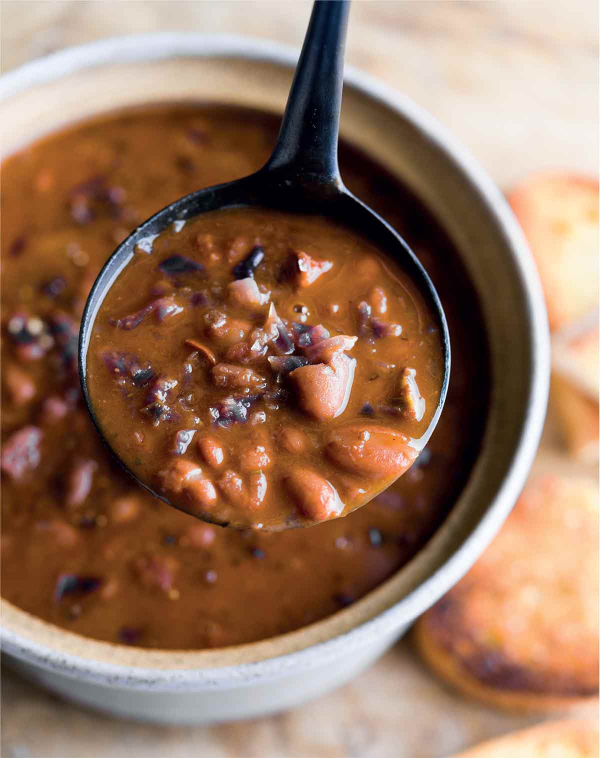 A ladle of braised cranberry beans with chorizo being held above a bowl.