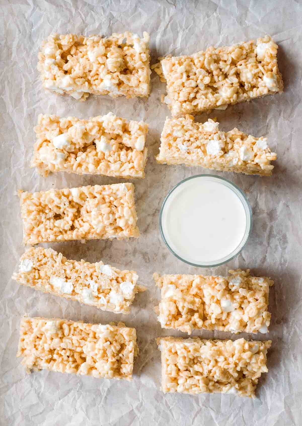 Nine brown butter rice krispies treats next to a glass of milk.