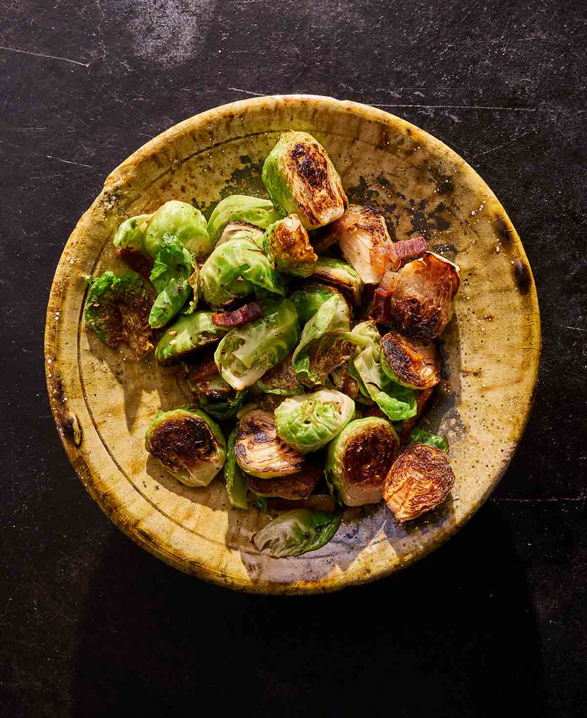 A wooden bowl filled with roasted Brussels sprouts with guanciale.