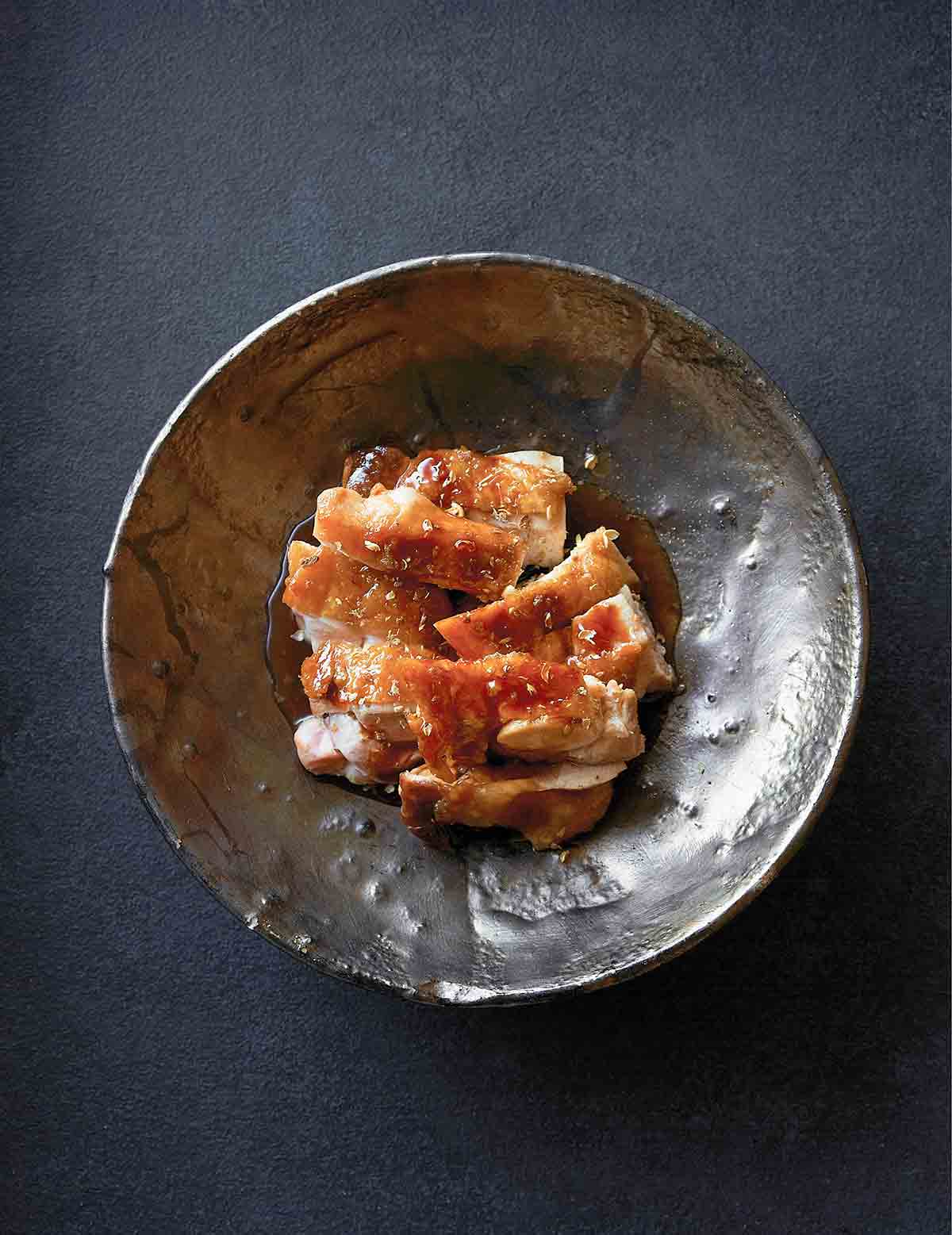 Pieces of sliced chicken with teriyaki sauce in a pewter bowl.