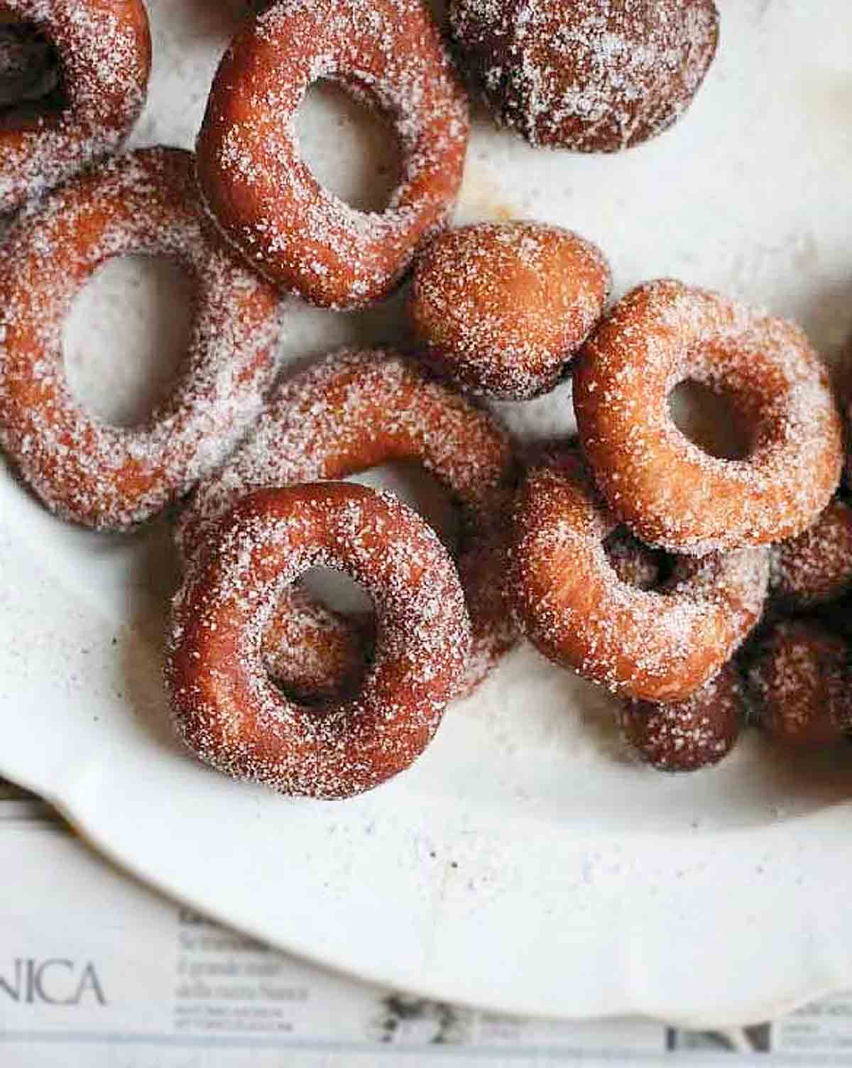 A pile of sugar-dusted easy raised doughnuts on a white plate.