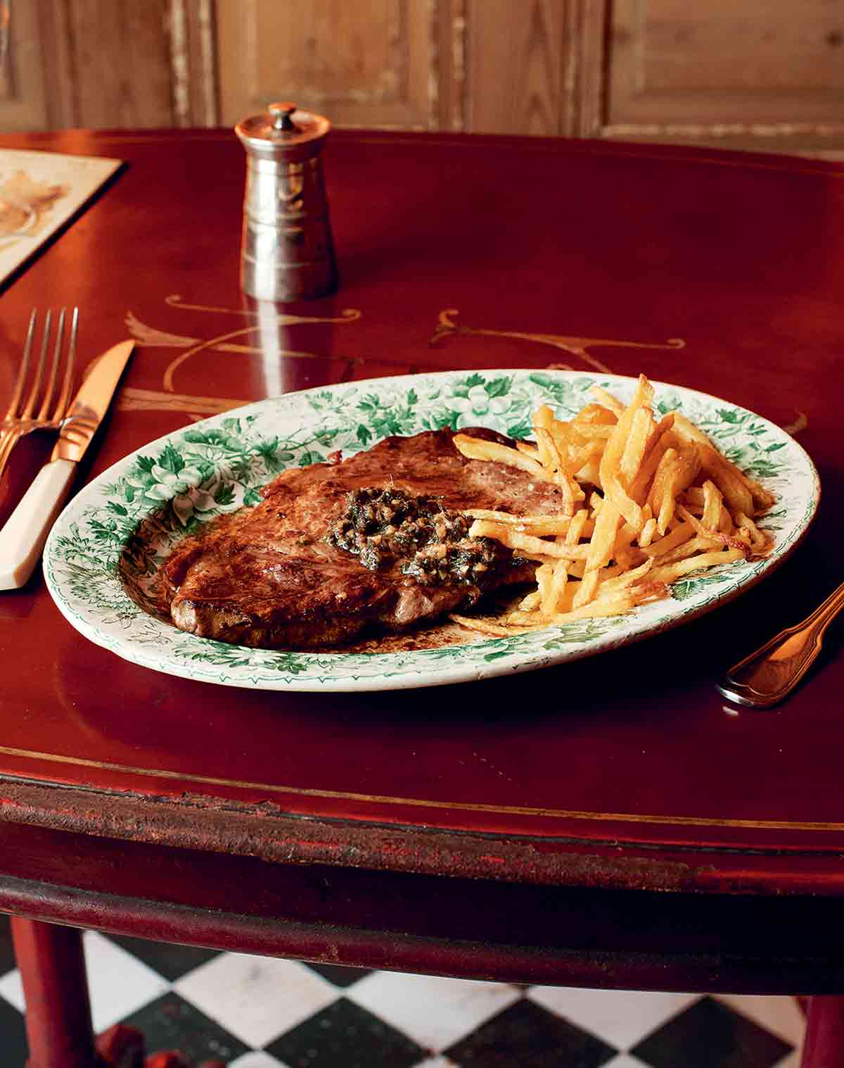 A green and white patterned plate filled with entrecôte à l'anchoïade and a pile of French fries