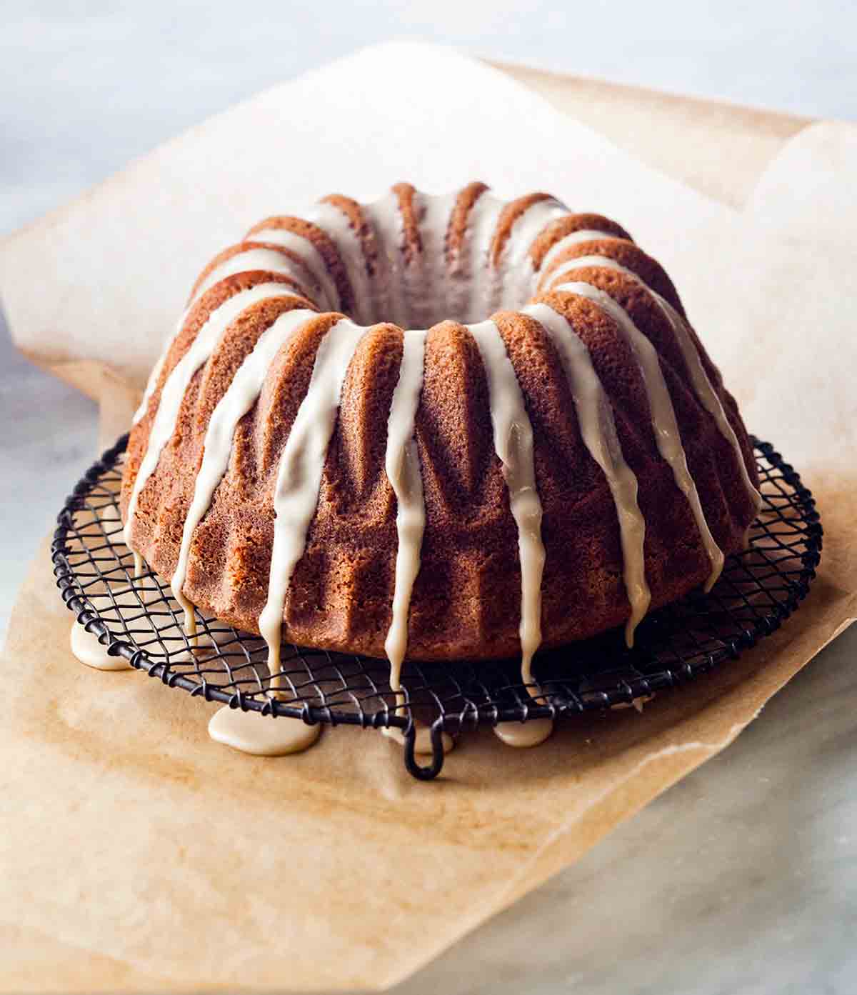 An espresso cake drizzled with glaze on a wire rack that is set on a pice of parchment to catch any glaze drips.