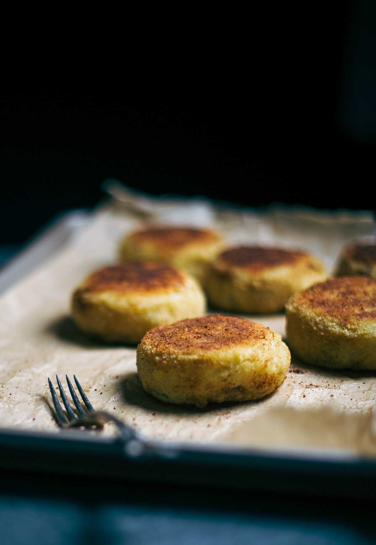 A sheet pan with six ground lamb and potato patties on parchment paper