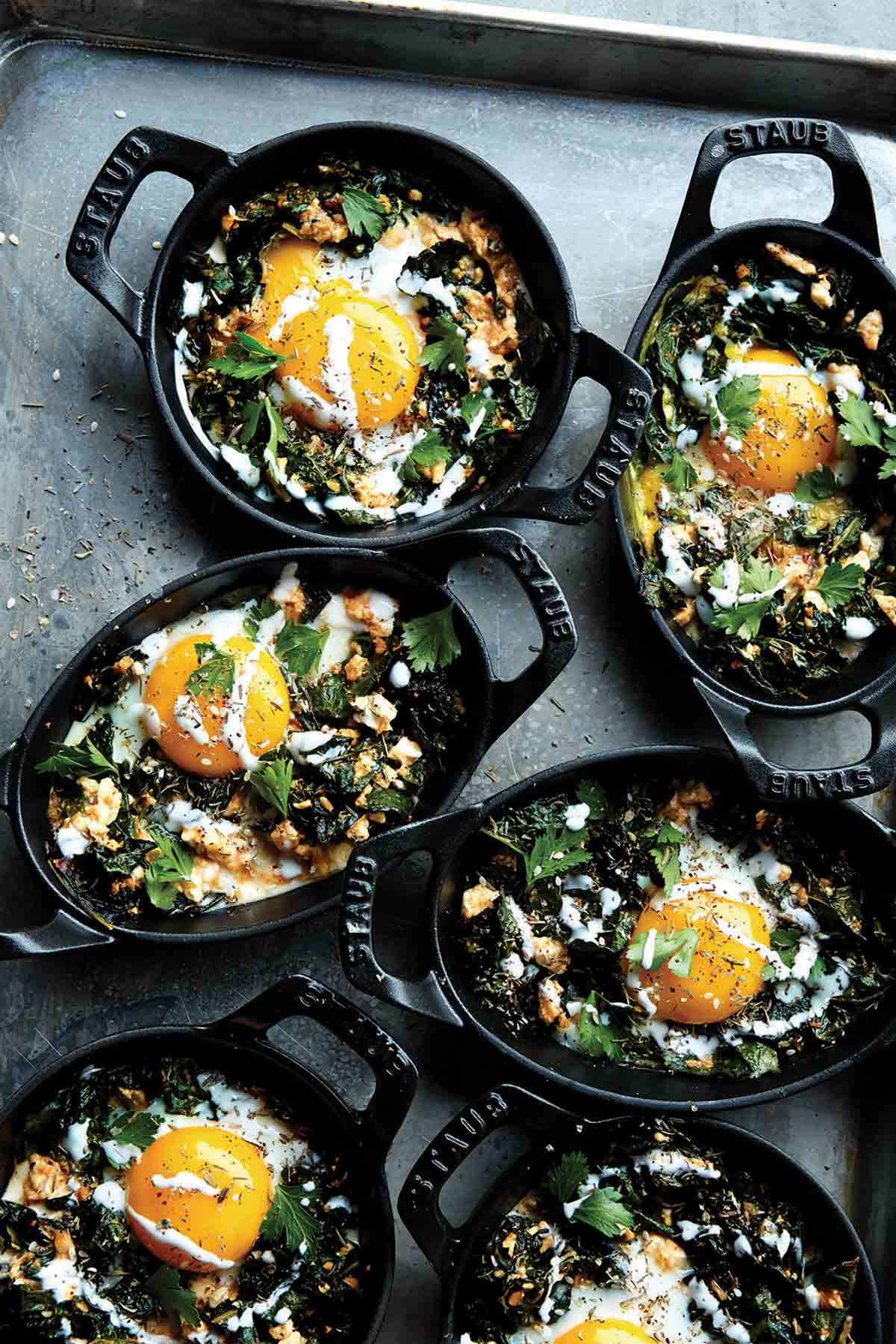 Mini Staub skillets filed with kale shakshuka--eggs, kale, and spices