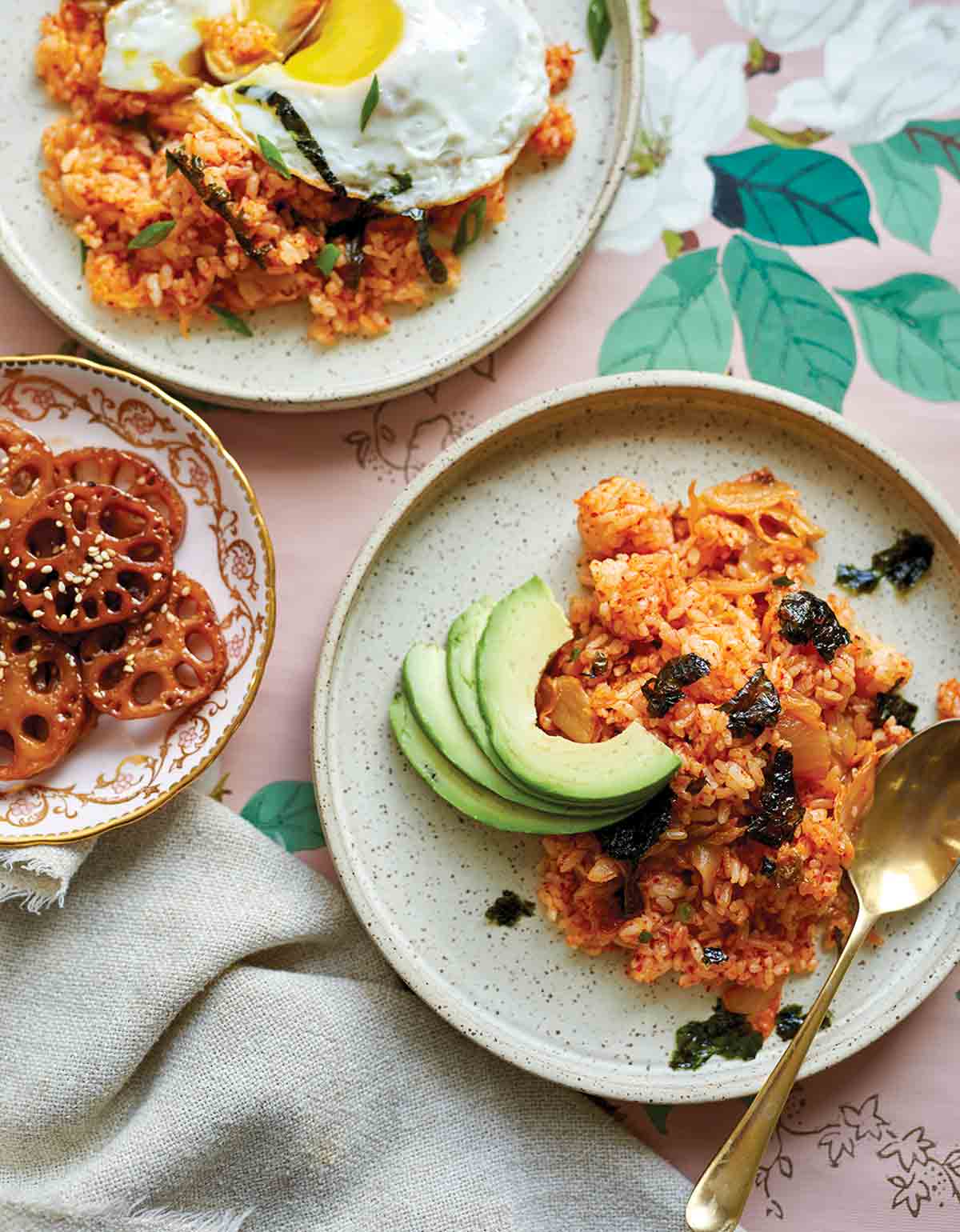 Two plates topped with kimchi fried rice and nori flakes, one with a fried egg and the other with sliced avocado.