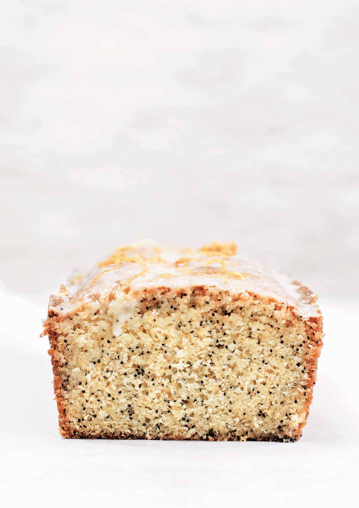 A cut loaf of lemon-poppy seed cake on a white background