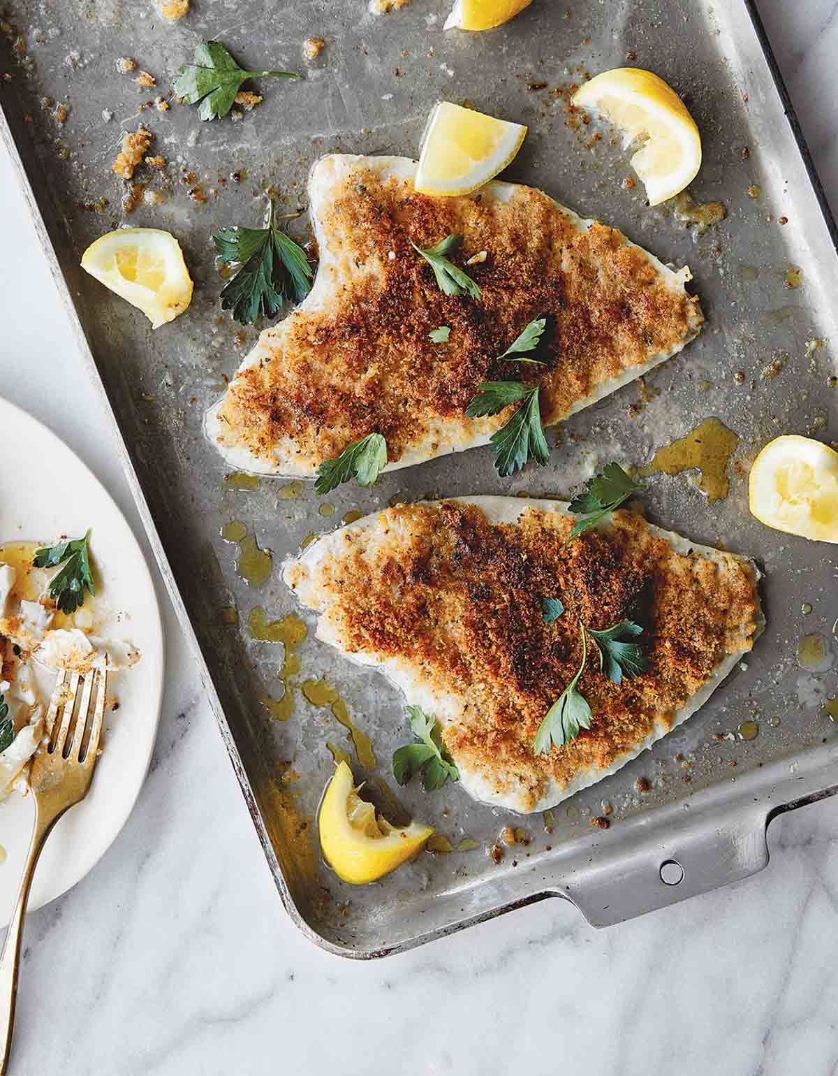 Two fillets of lemon sole oreganata topped with a Parmigiano-Reggiano breadcrumb mixture on a baking sheet