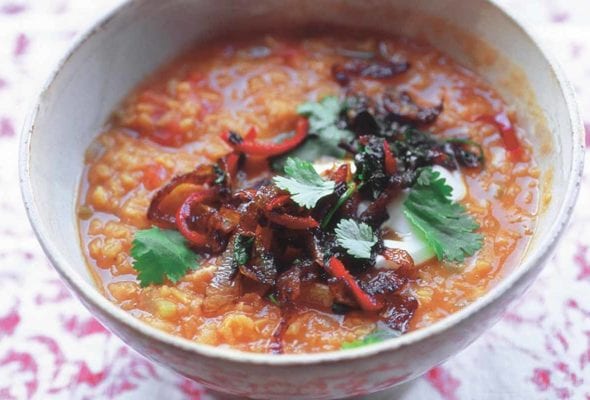 A white bowl filled with lentil soup and topped with fried chiles, greek yogurt, and cilantro
