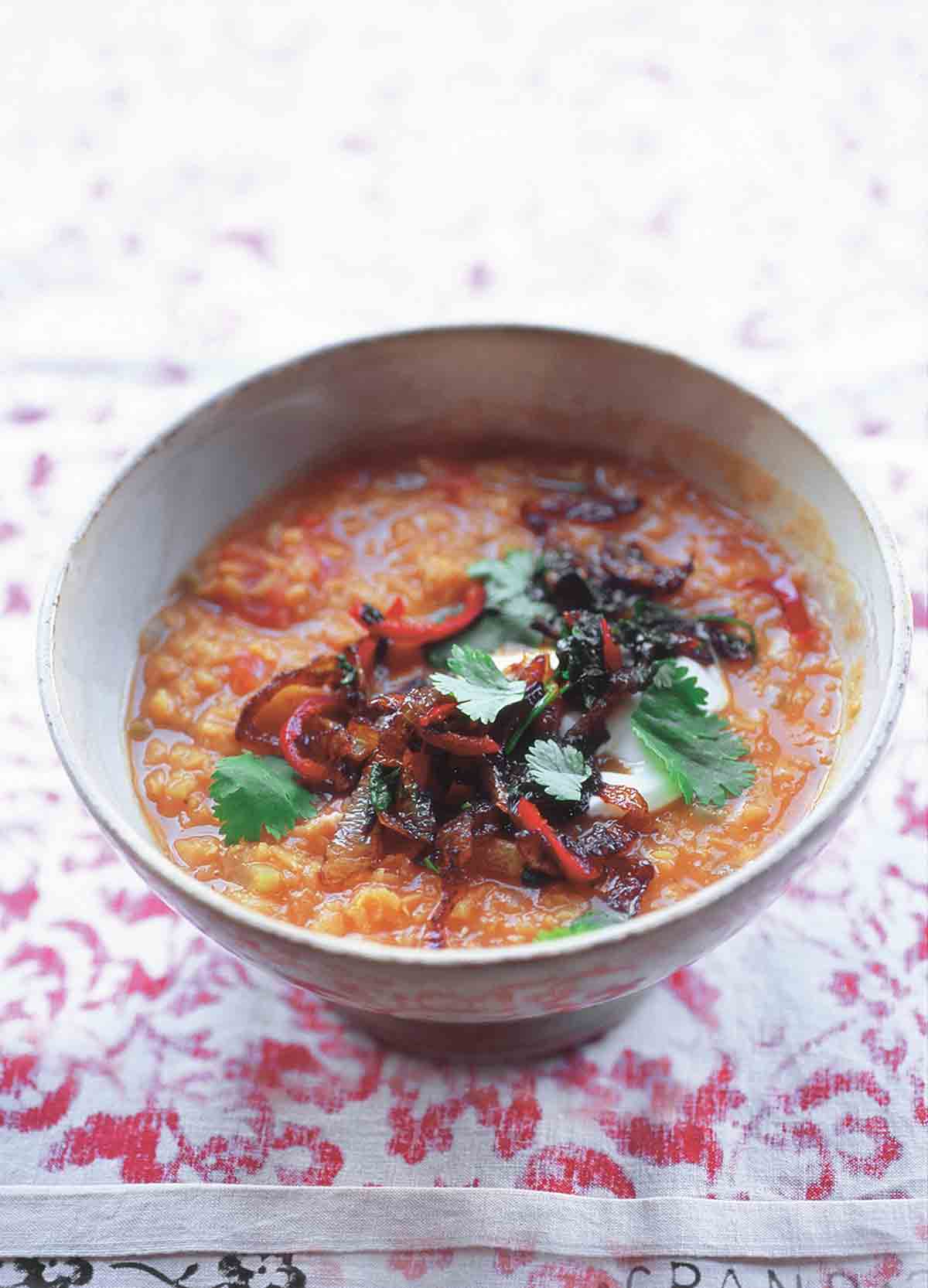 A white bowl filled with lentil soup and topped with fried chiles, greek yogurt, and cilantro