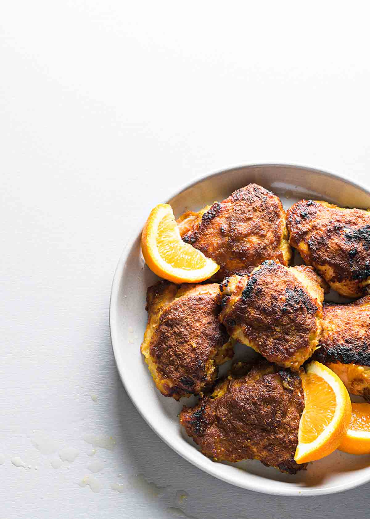A white plate filled with orange ginger chicken thighs and orange wedges.