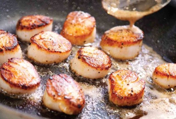 A skillet filled with pan seared scallops cooked in butter