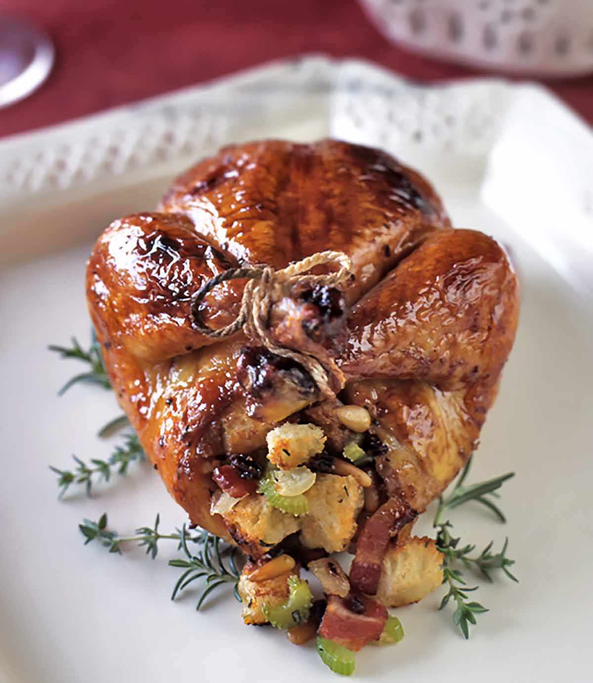 A stuffed pomegranate-glazed Cornish game hen on a white platter