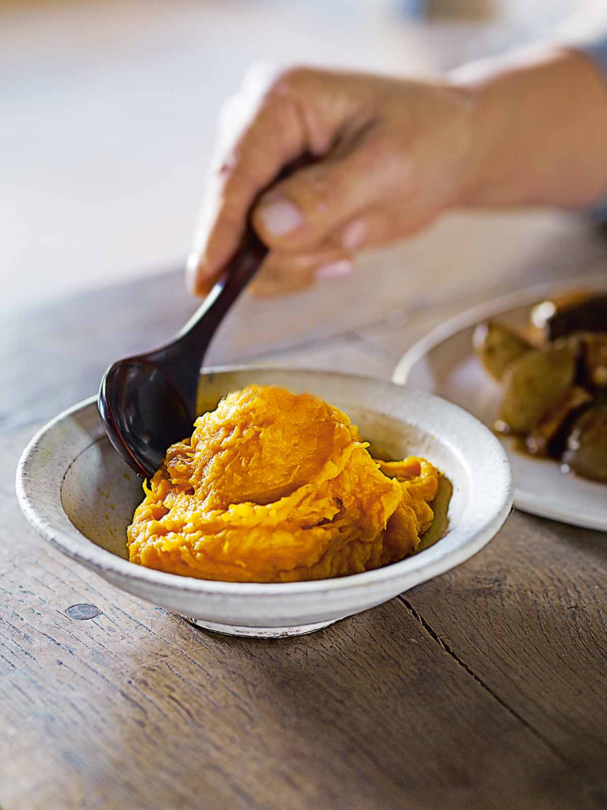 A ceramic bowl filled with pumpkin ginger mash with a person scooping a spoon into it.