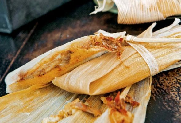 Two wrapped tamales on top of an open corn husk