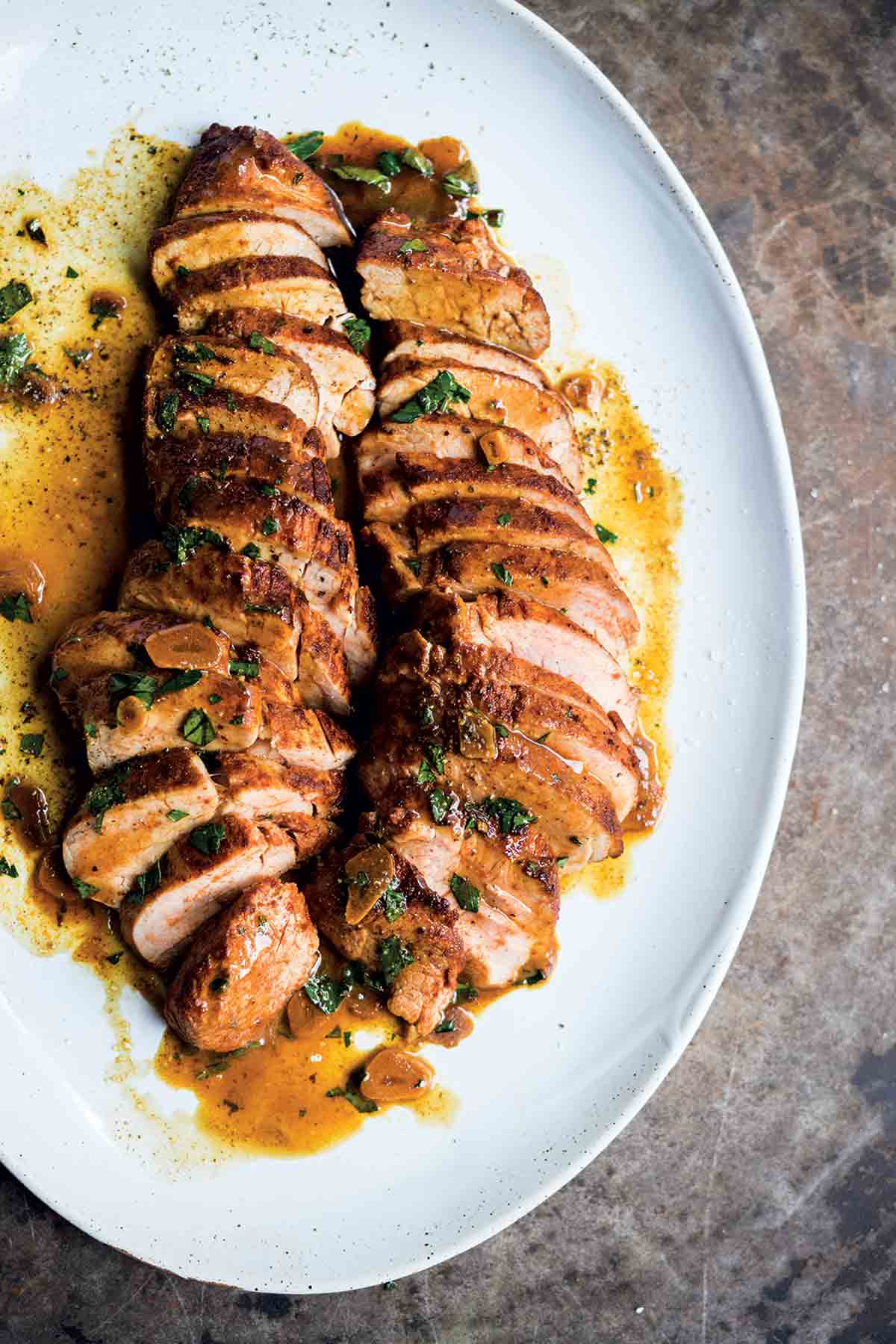 White plate of sliced pork tenderloin with paprika drizzled with a garlic butter sauce